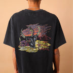 Person wearing a black t-shirt with a colorful graphic design on the back, standing against a beige wall.