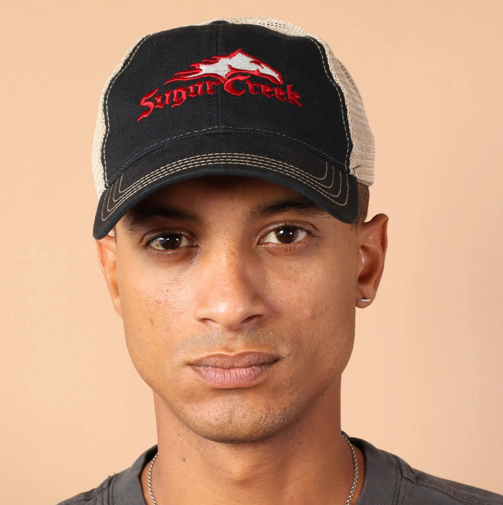 Man wearing a black cap with a logo and gray shirt against a beige background