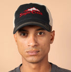 Man wearing a black cap with a logo and gray shirt against a beige background