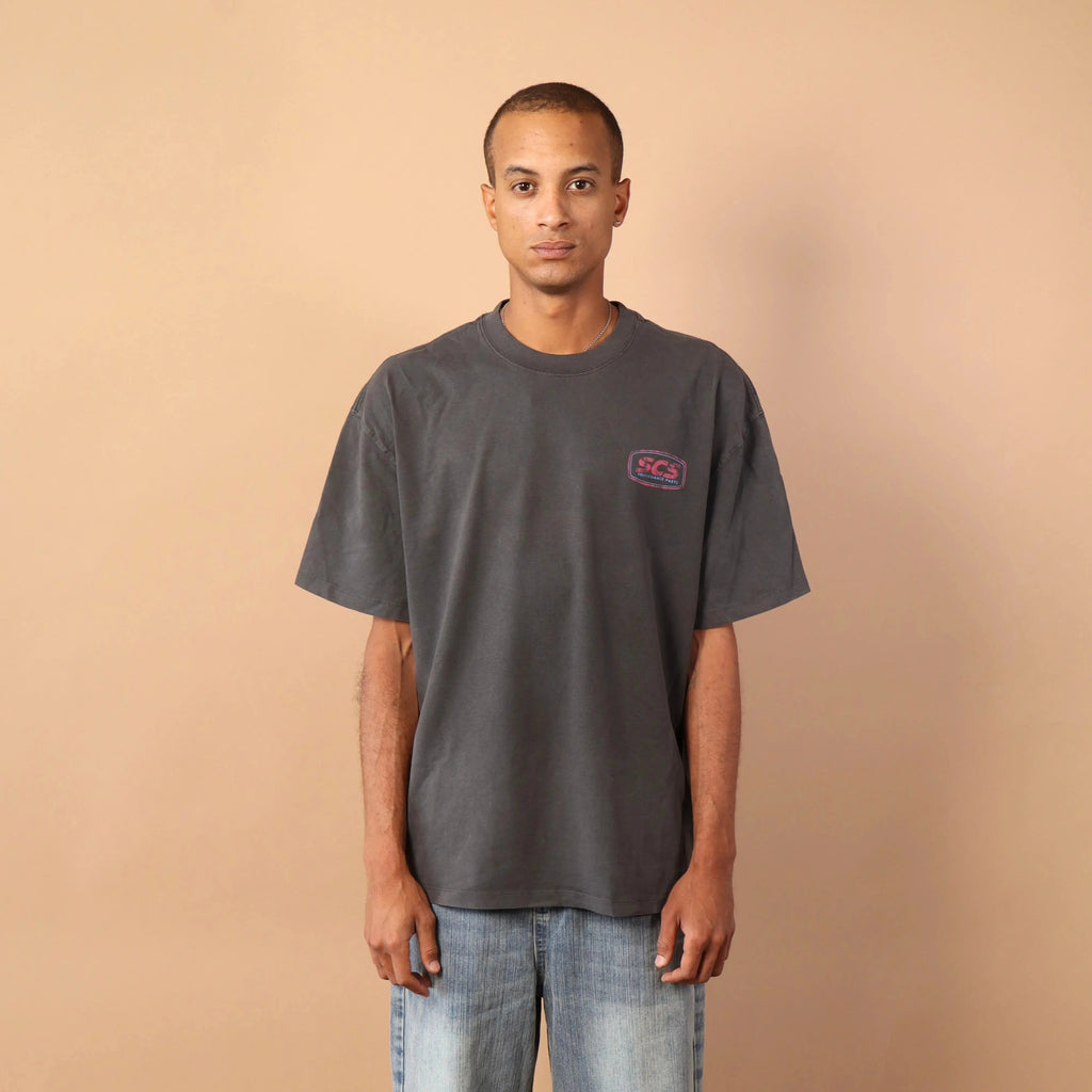Person wearing a gray t-shirt and blue jeans standing against a beige wall.