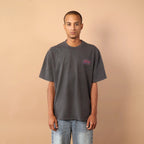 Person wearing a gray t-shirt and blue jeans standing against a beige wall.