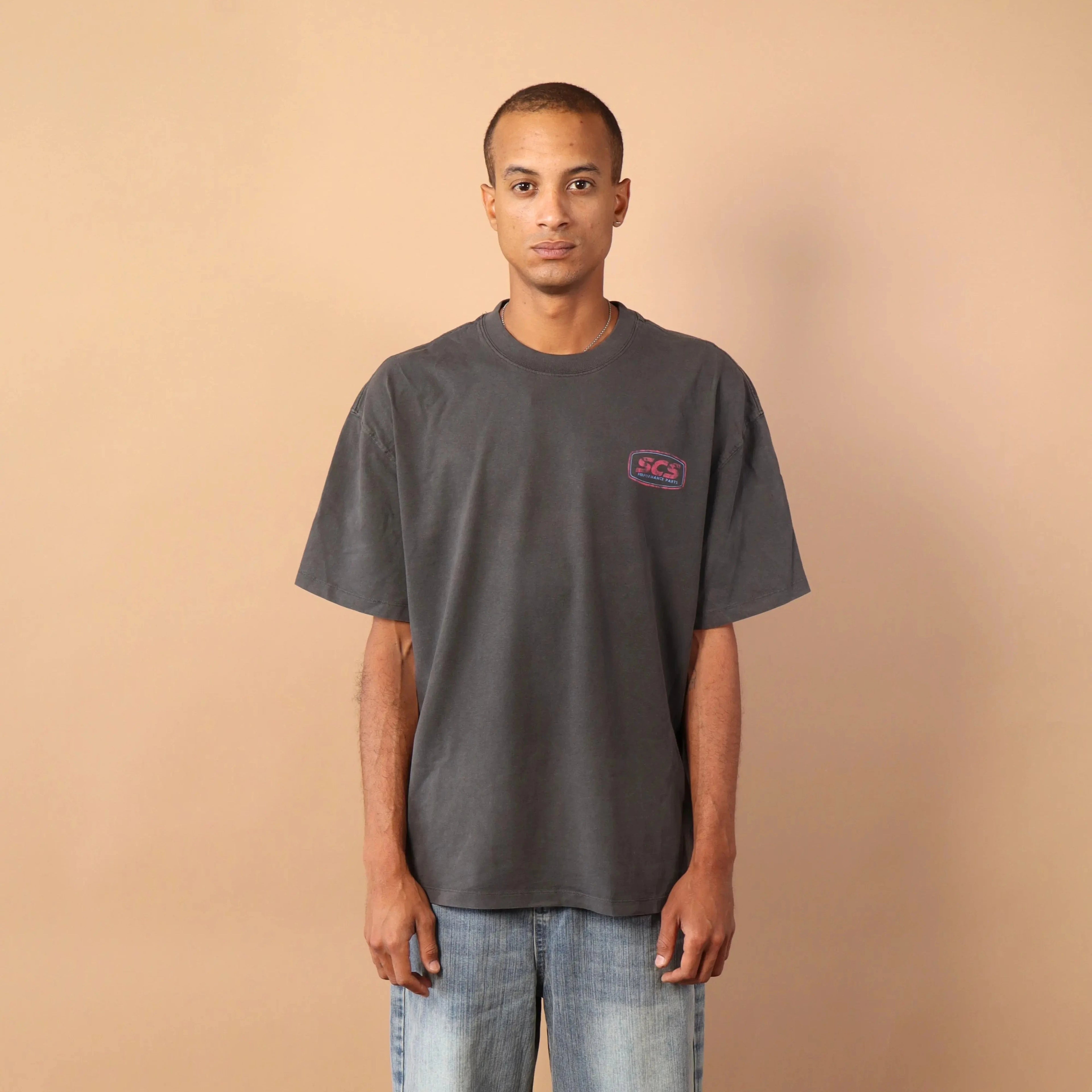 Person wearing a gray t-shirt and blue jeans standing against a beige wall.