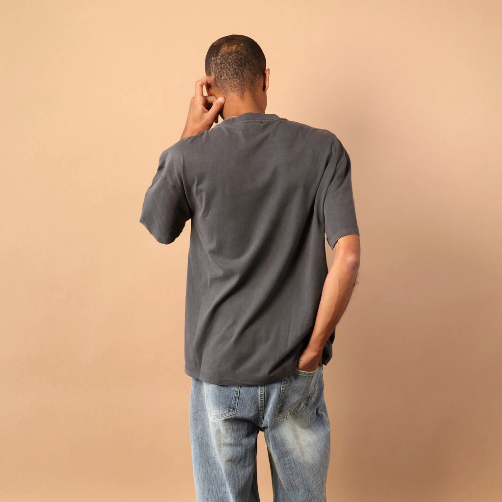 Person wearing a gray t-shirt and blue jeans against a beige wall.