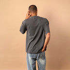 Person wearing a gray t-shirt and blue jeans against a beige wall.
