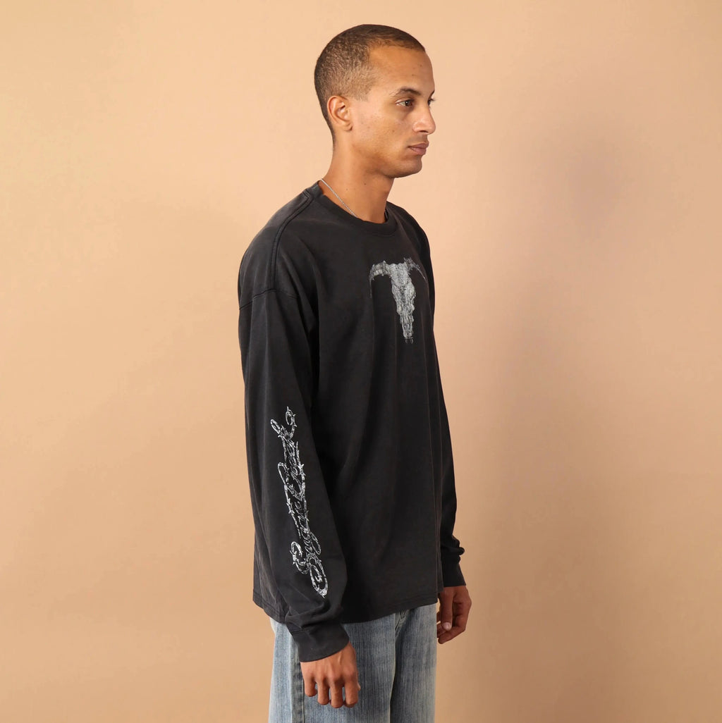 Man wearing a black long-sleeve shirt and light blue jeans standing against a beige background