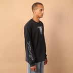 Man wearing a black long-sleeve shirt and light blue jeans standing against a beige background