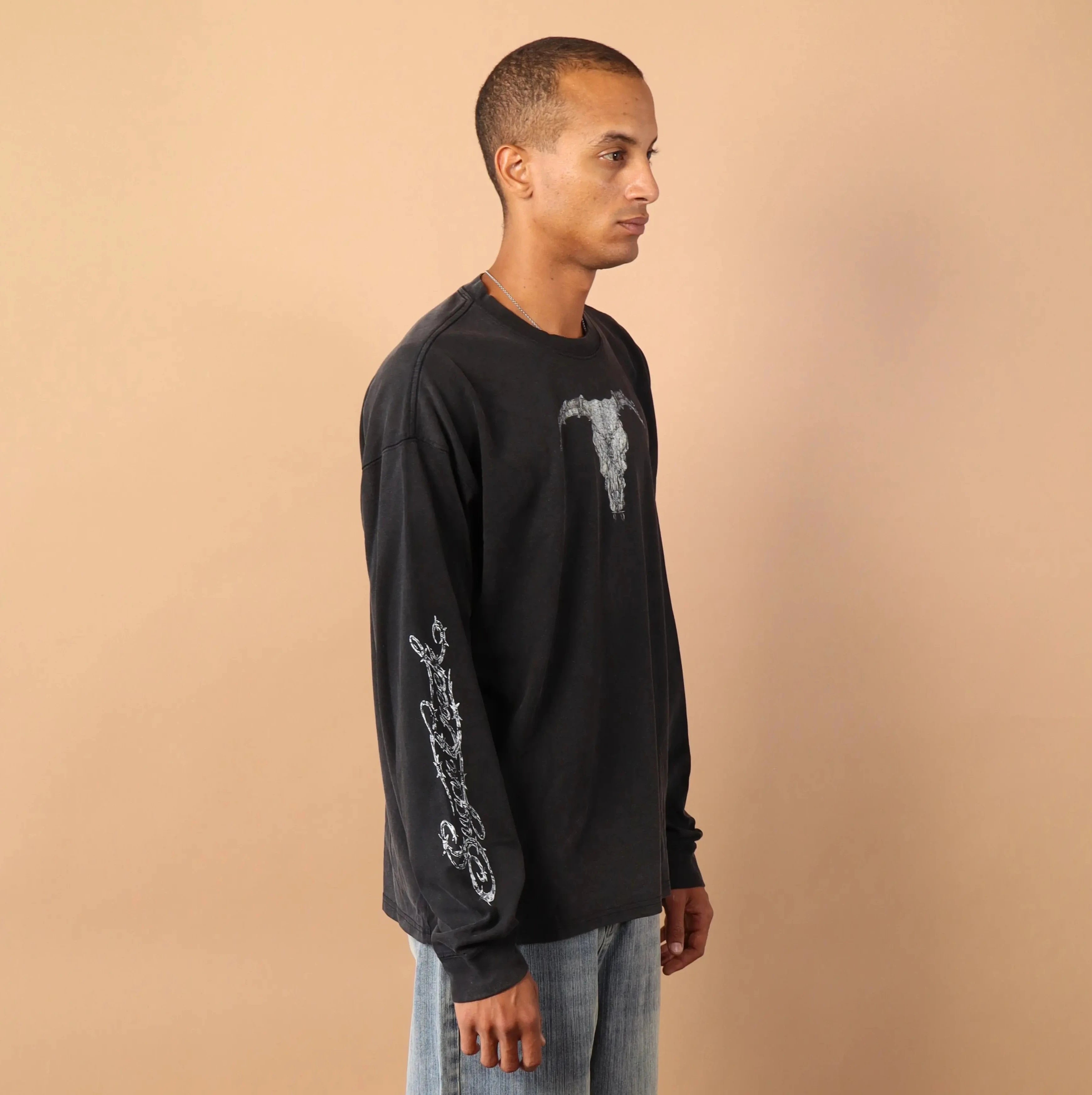 Man wearing a black long-sleeve shirt and light blue jeans standing against a beige background