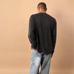 Person wearing a black long-sleeve shirt and light blue jeans against a beige wall.