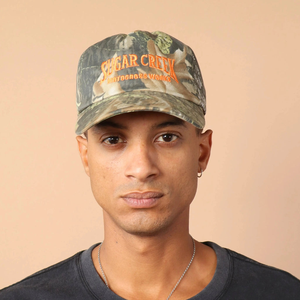 Person wearing a camouflage cap with text on a beige background
