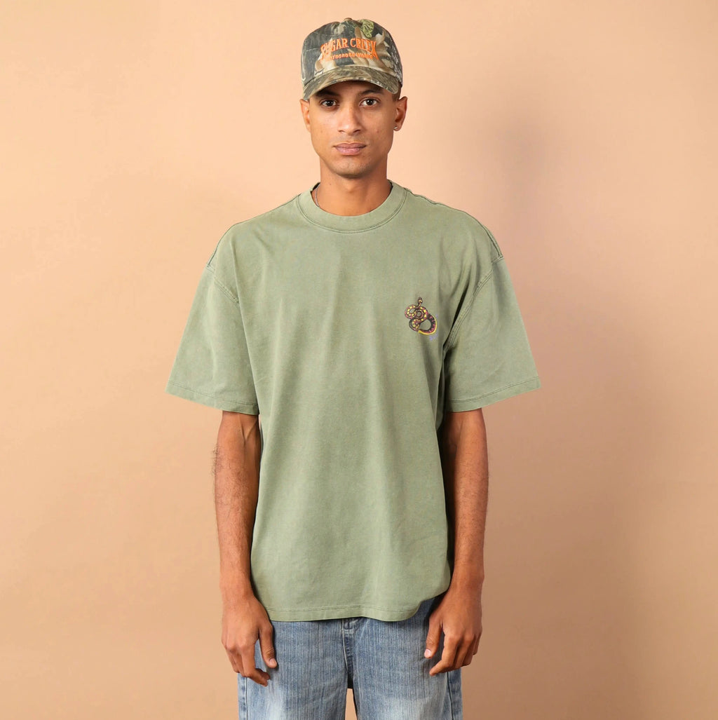 Person wearing a green t-shirt and camouflage cap against a beige background