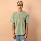 Person wearing a green t-shirt and camouflage cap against a beige background