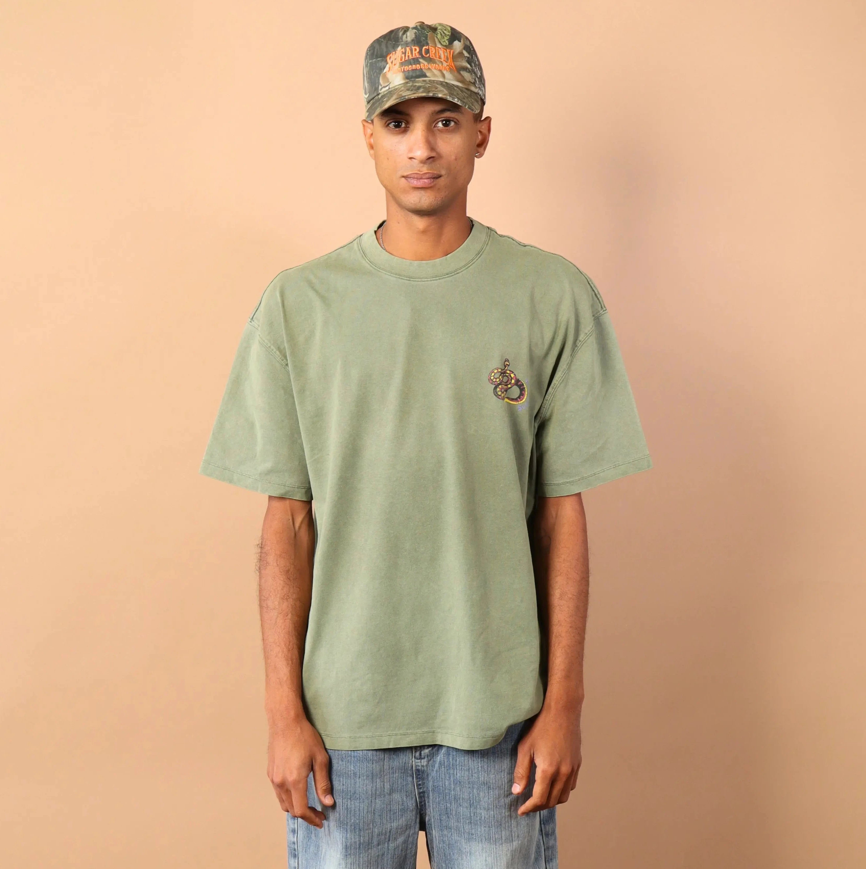 Person wearing a green t-shirt and camouflage cap against a beige background