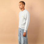 Person wearing a light gray sweater and light blue jeans against a beige wall.