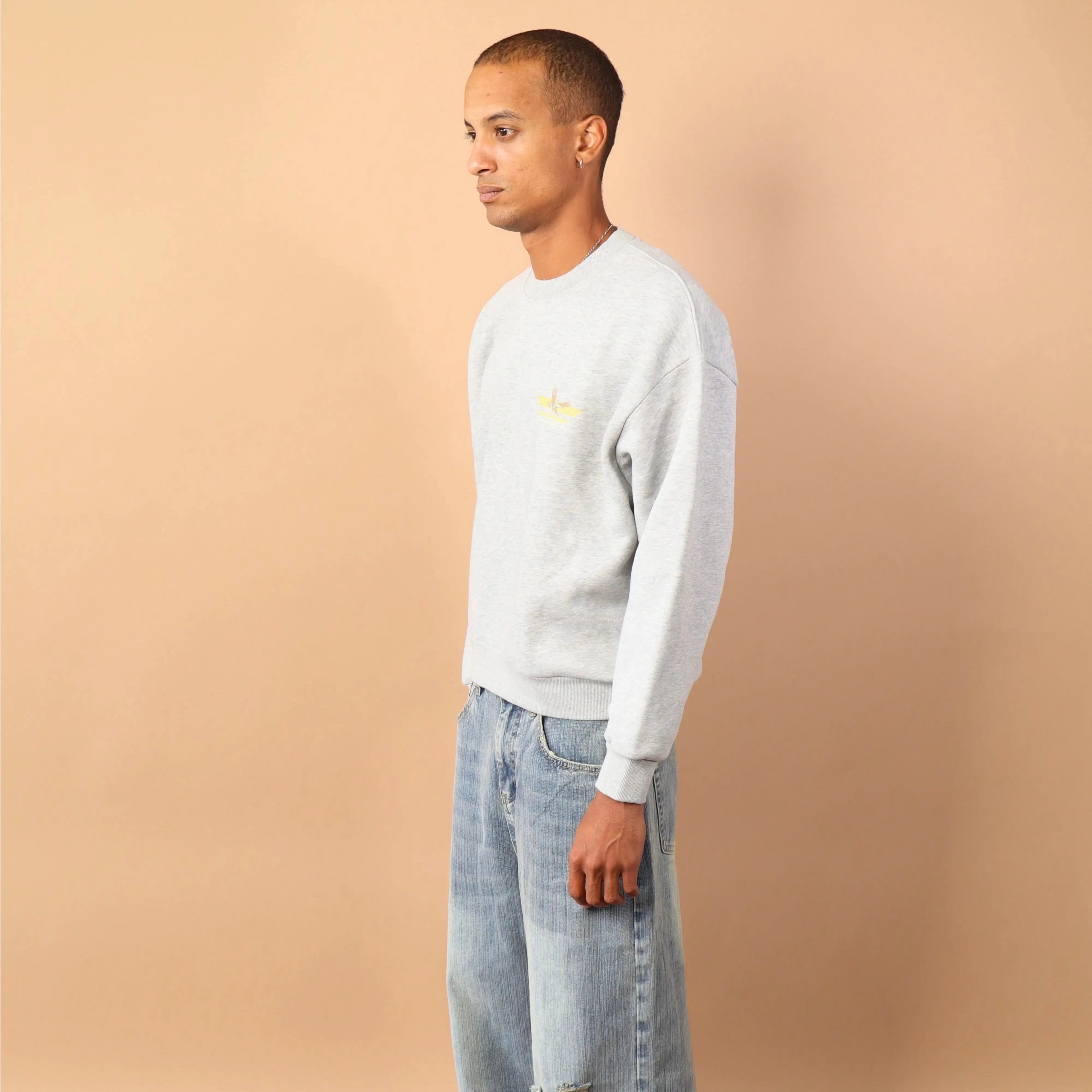 Person wearing a light gray sweater and light blue jeans against a beige wall.