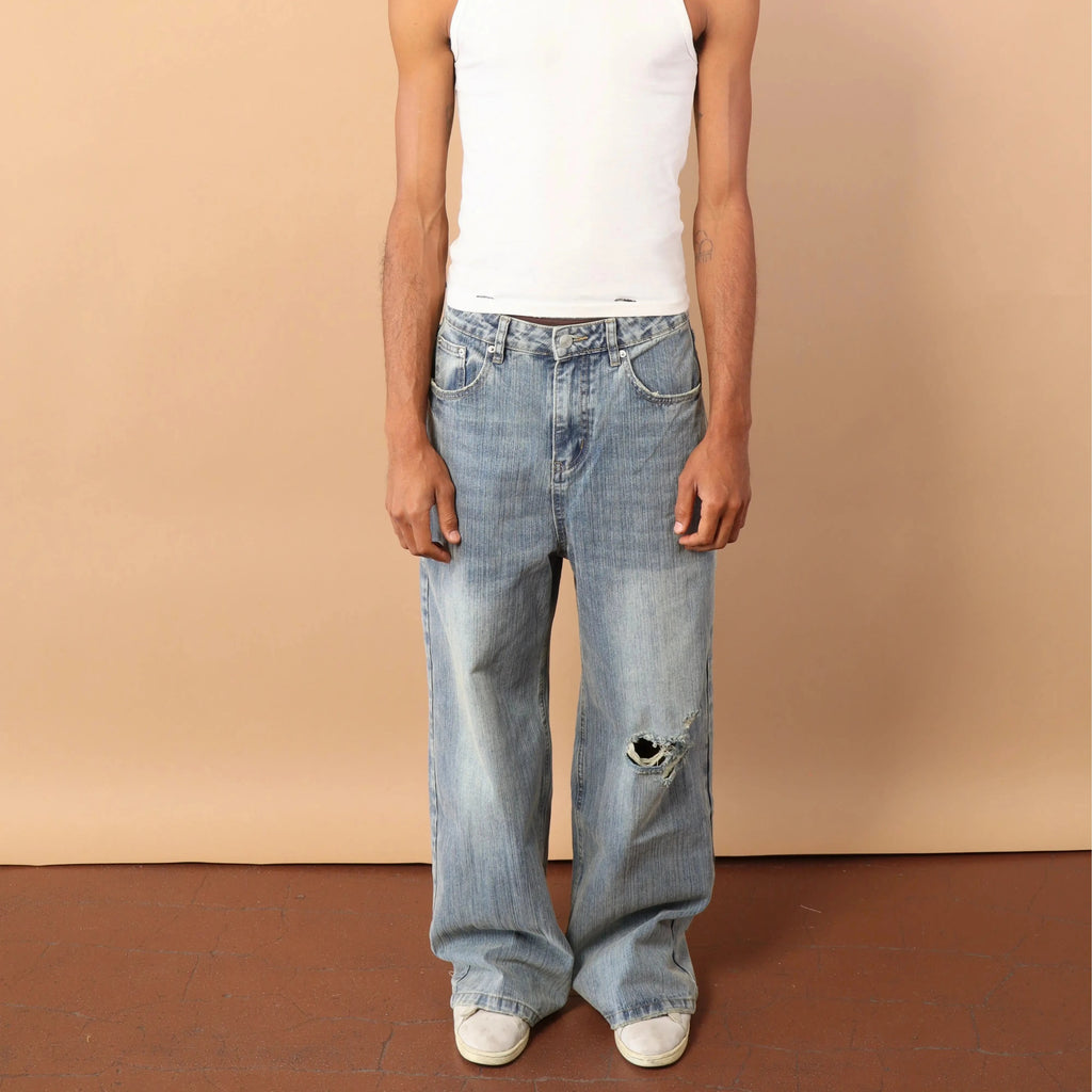 Man wearing a white tank top and blue jeans against a beige background