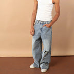 Man wearing a white tank top and blue jeans against a beige background
