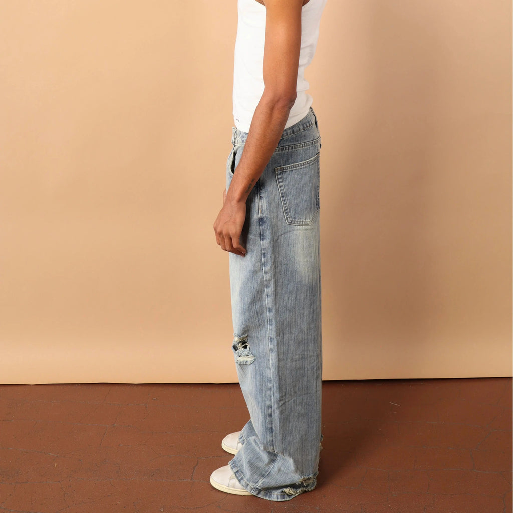 Person wearing a white tank top and light blue jeans against a beige wall.