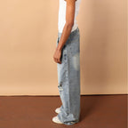 Person wearing a white tank top and light blue jeans against a beige wall.