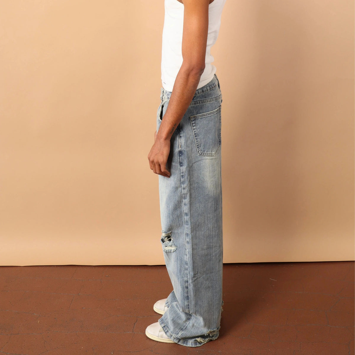 Person wearing a white tank top and light blue jeans against a beige wall.