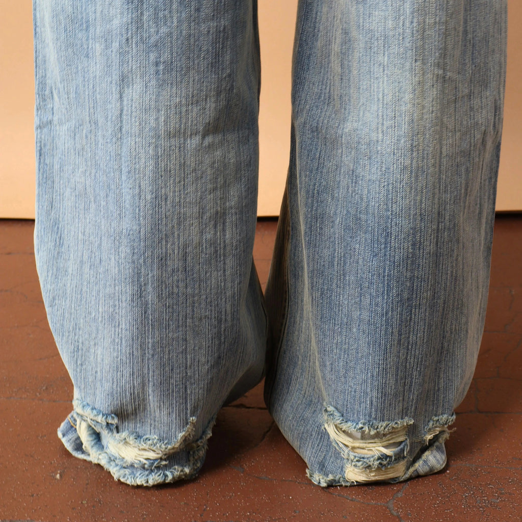 Blue jeans with frayed cuffs on a brown floor.