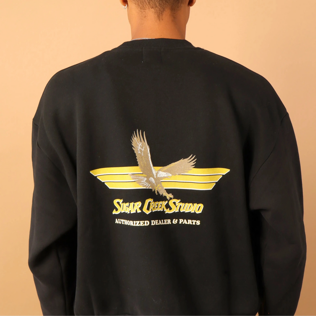 Person wearing a black sweatshirt with a logo on the back against a beige background