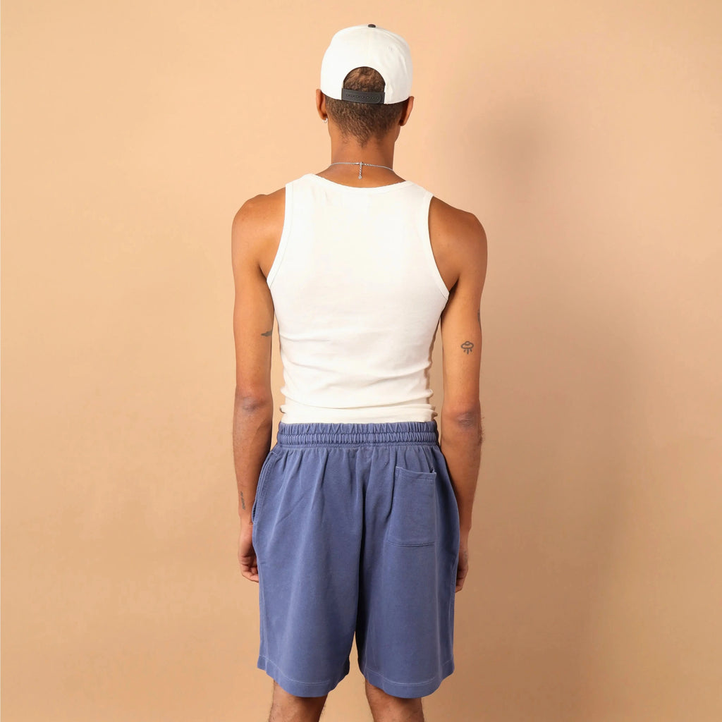 Person wearing a white tank top, blue shorts, and a white cap on a beige background