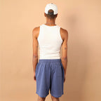 Person wearing a white tank top, blue shorts, and a white cap on a beige background