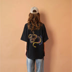 Person wearing a black t-shirt with a snake design, standing against a peach wall.