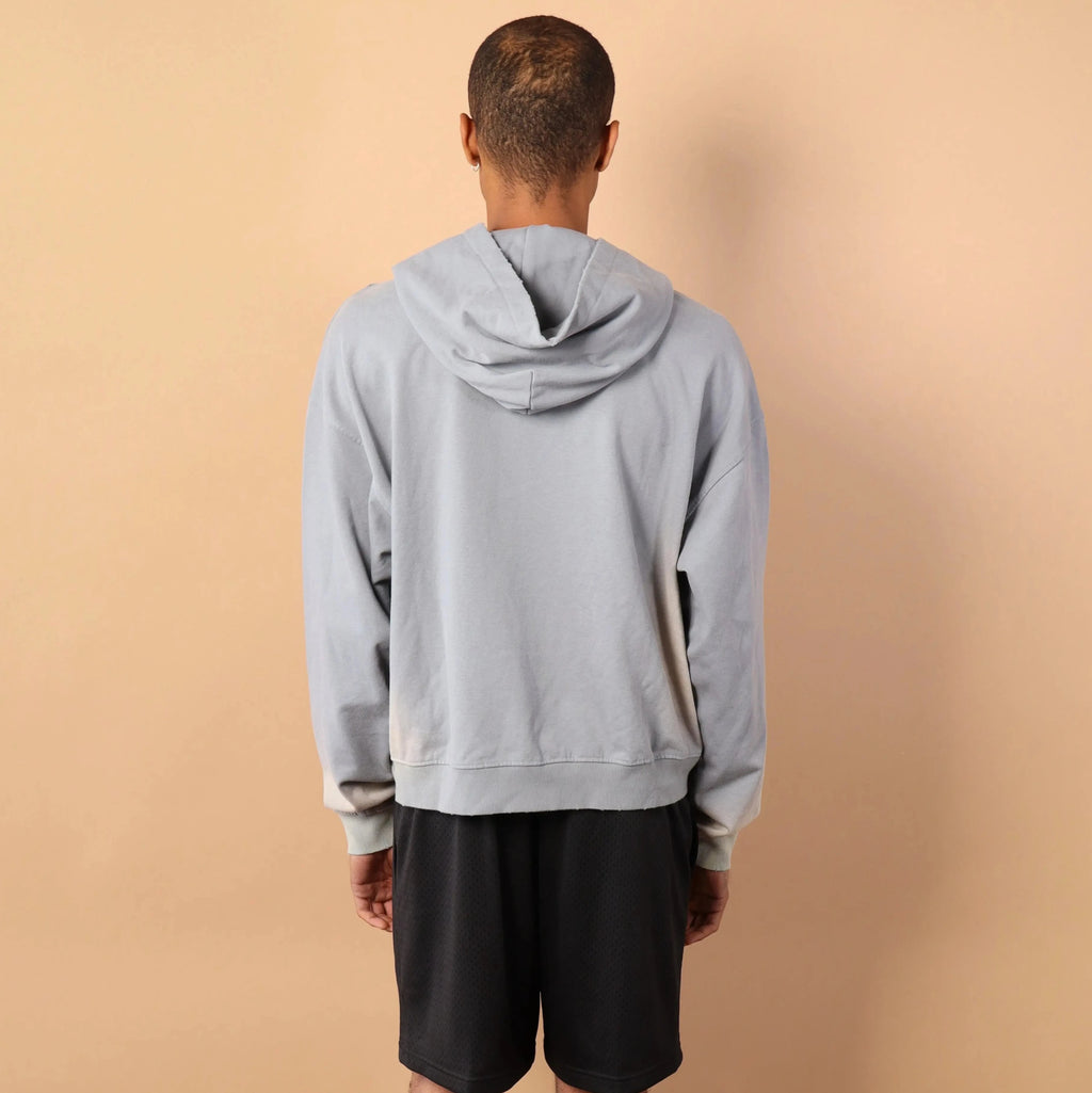 Person wearing a gray hoodie and black shorts standing against a beige wall.