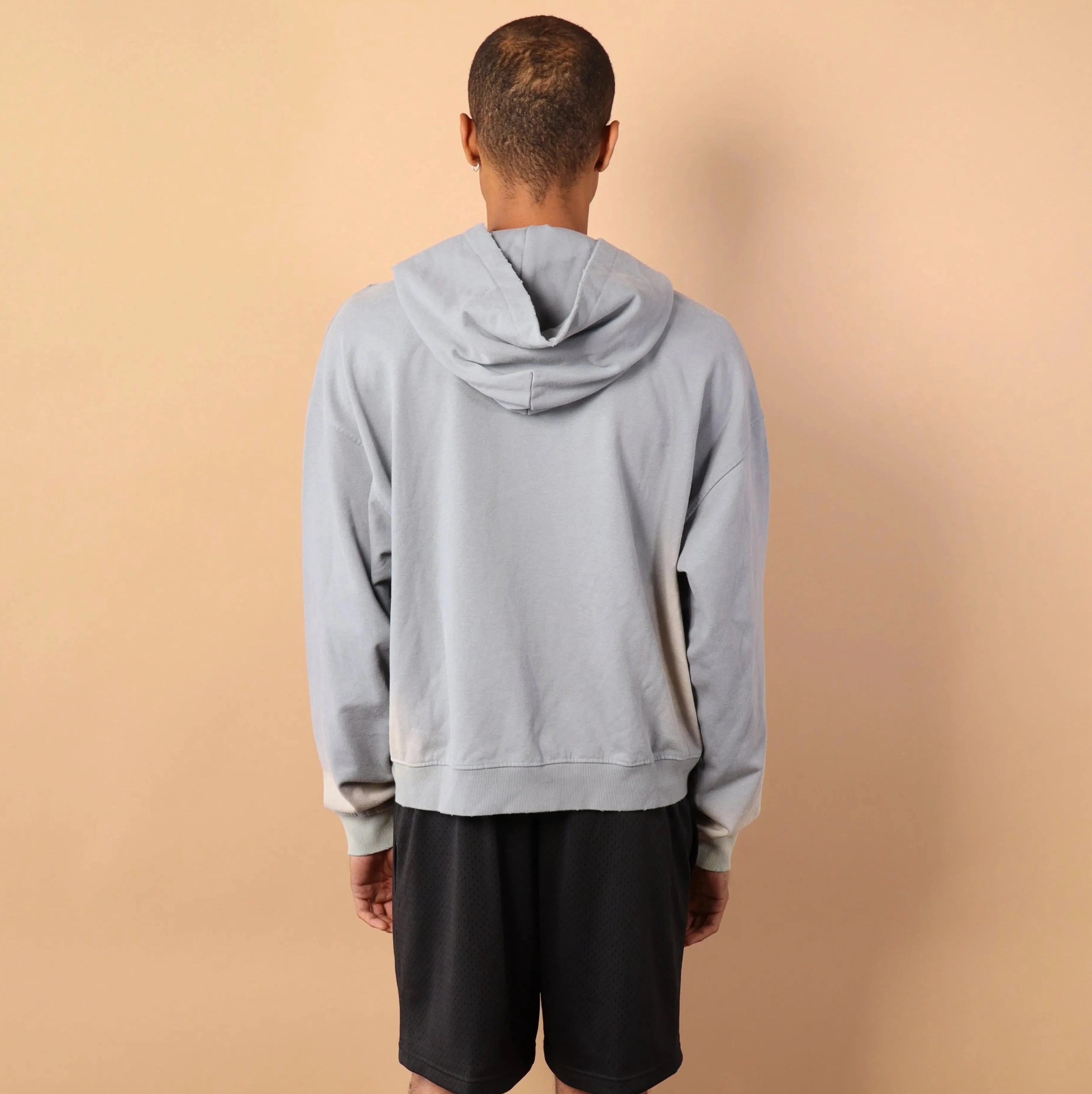 Person wearing a gray hoodie and black shorts standing against a beige wall.