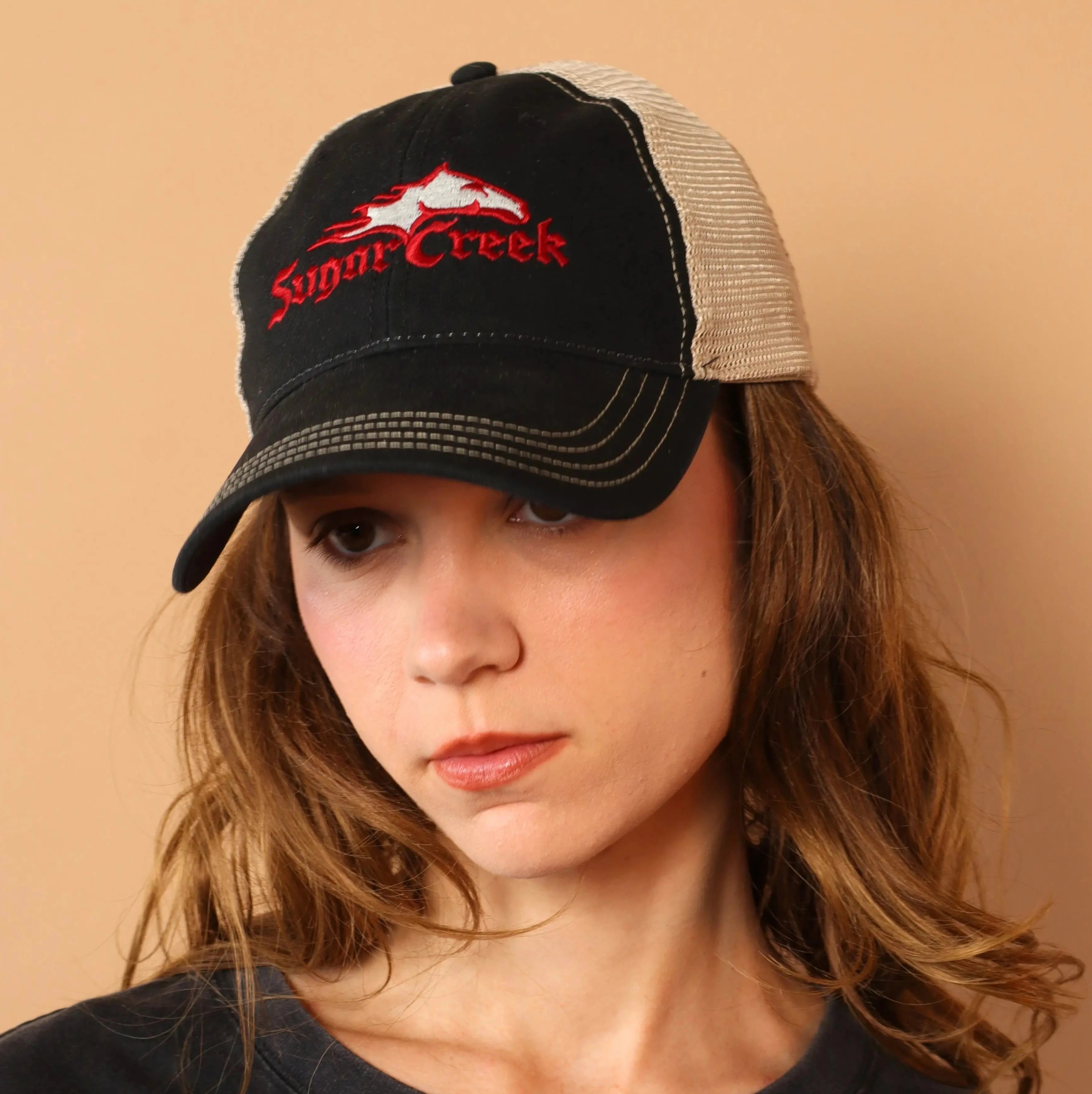 Person wearing a black cap with red logo on a beige background