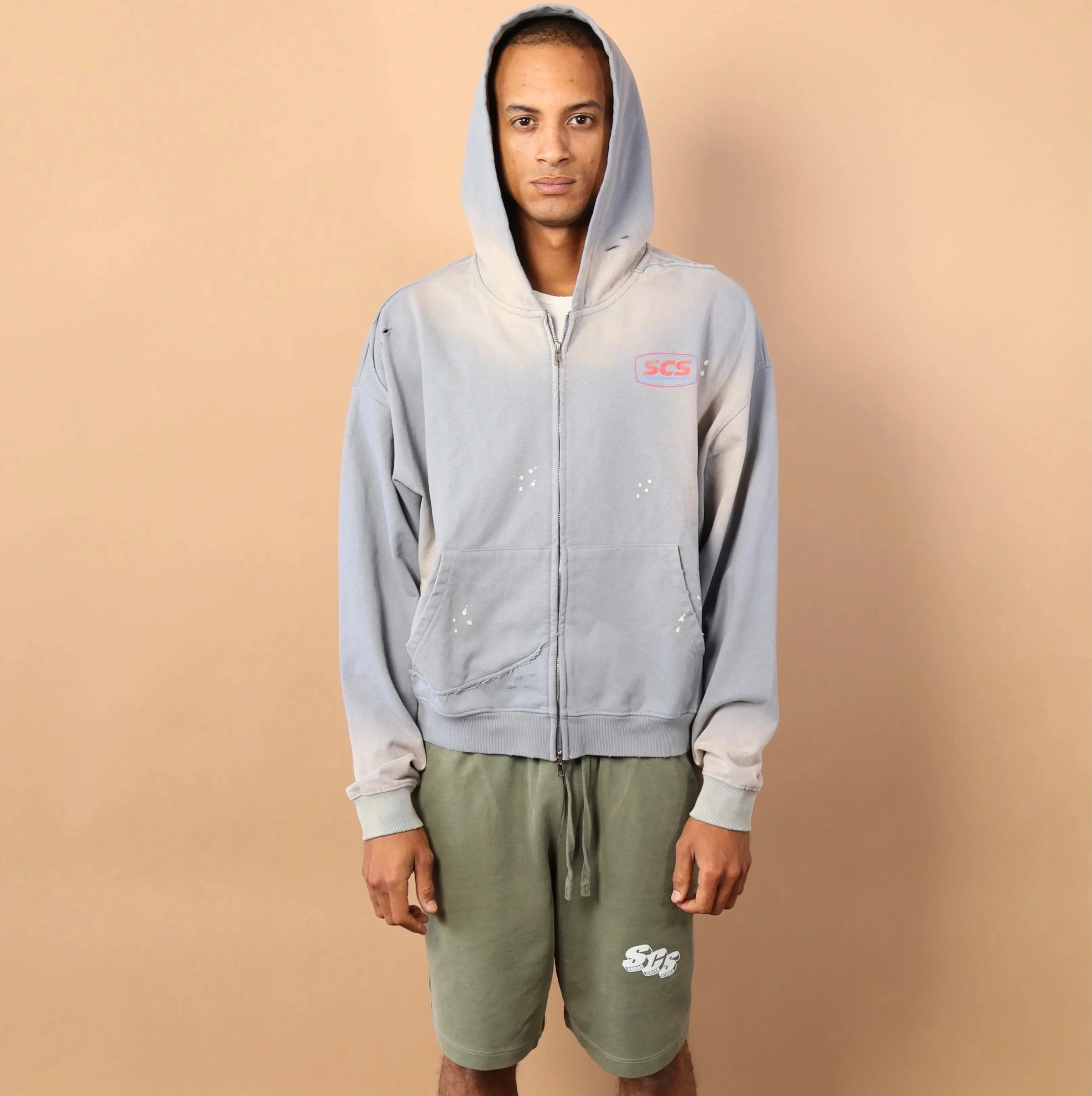 Person wearing a light gray hoodie and green shorts against a beige background