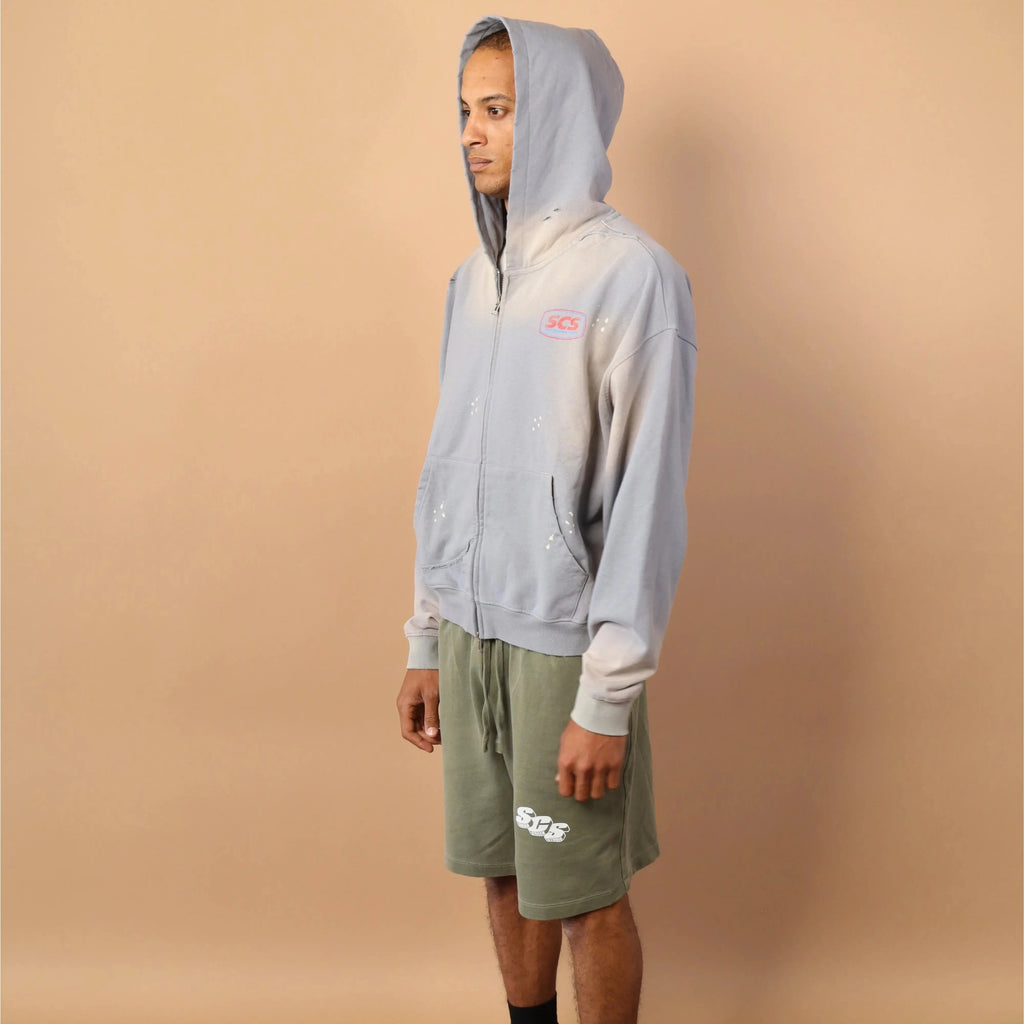 Person wearing a light gray hoodie and green shorts against a beige background