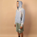 Person wearing a light gray hoodie and green shorts against a beige background