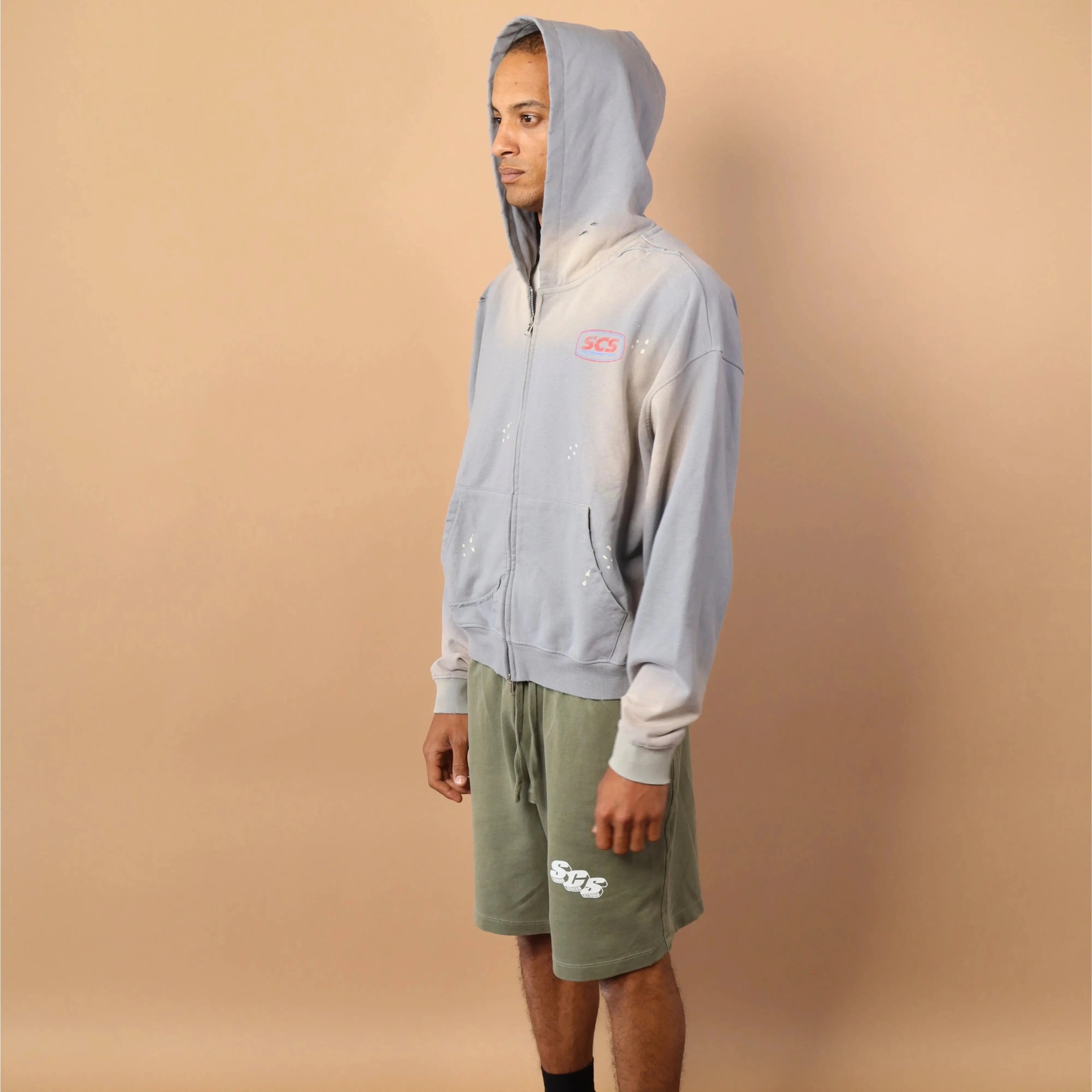 Person wearing a light gray hoodie and green shorts against a beige background