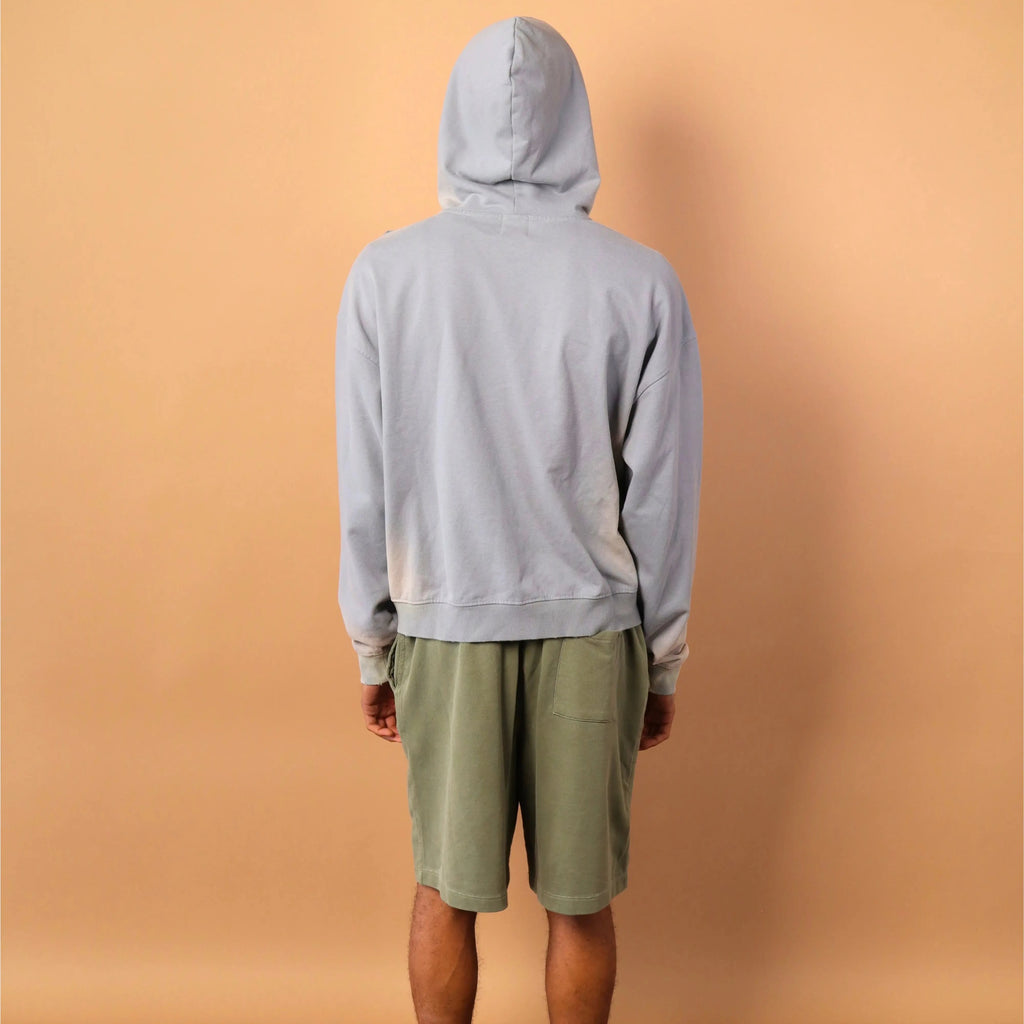 Person wearing a gray hoodie and green shorts standing against a beige wall.