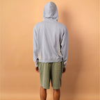 Person wearing a gray hoodie and green shorts standing against a beige wall.