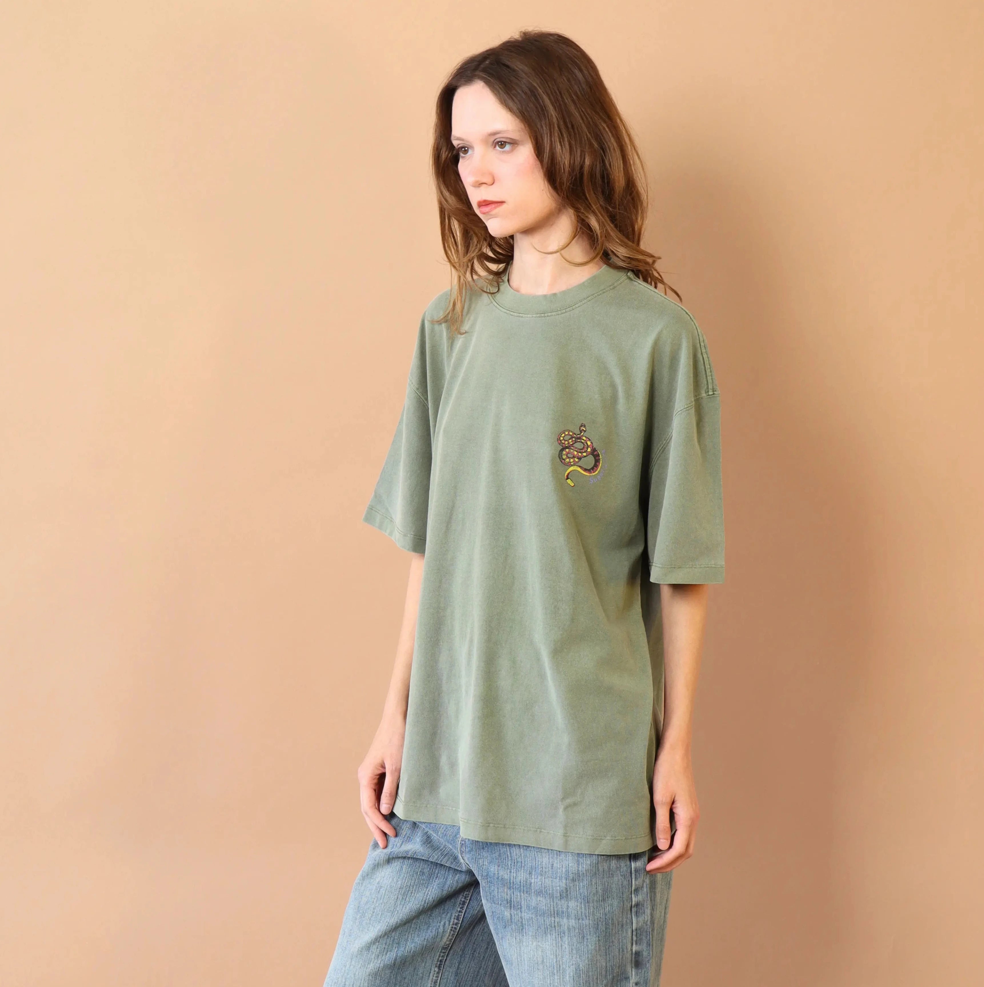 Person wearing a green t-shirt and blue jeans against a beige wall.