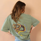 Person wearing a green t-shirt with a colorful snake design on the back against a beige background