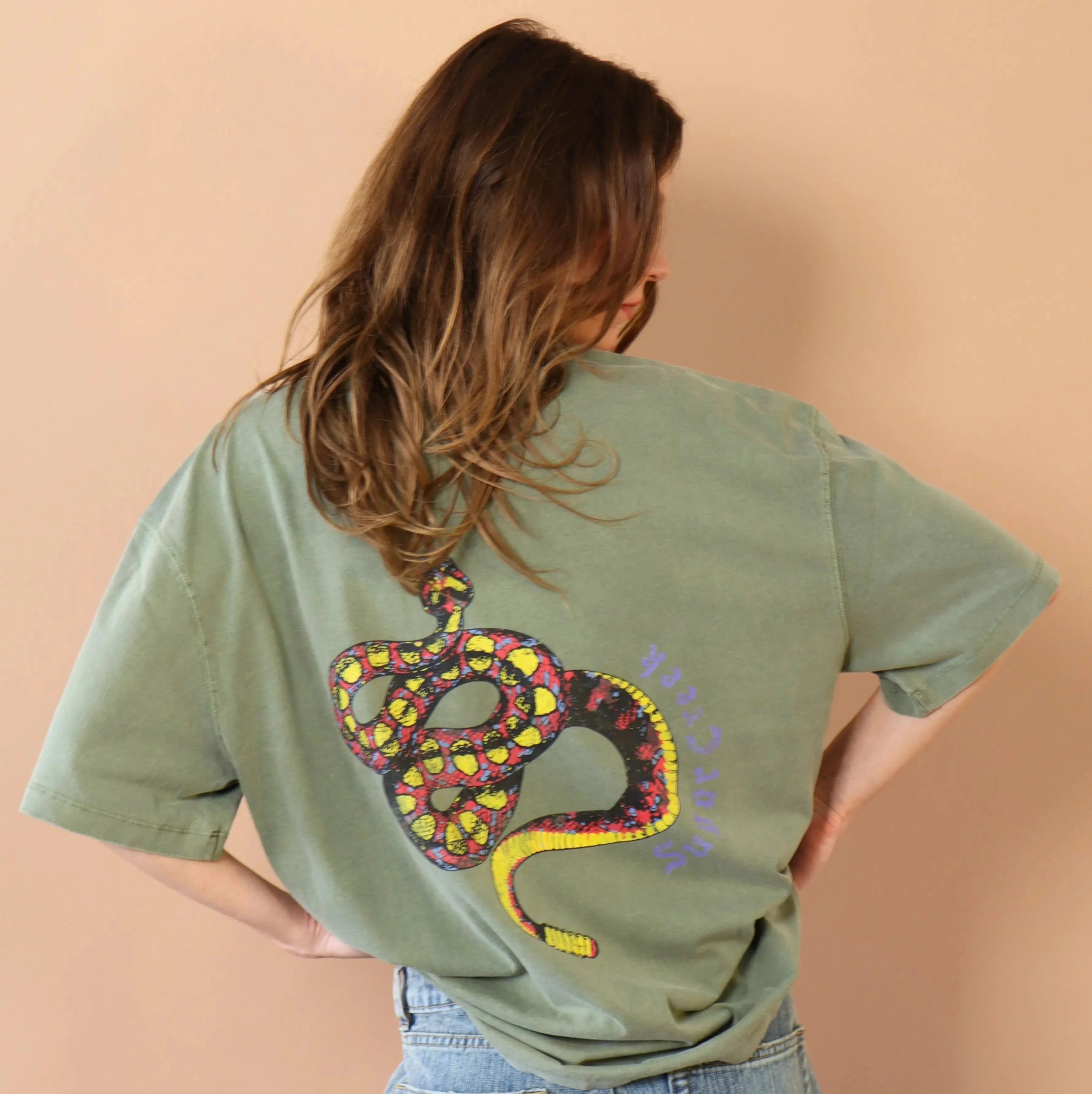 Person wearing a green t-shirt with a colorful snake design on the back against a beige background