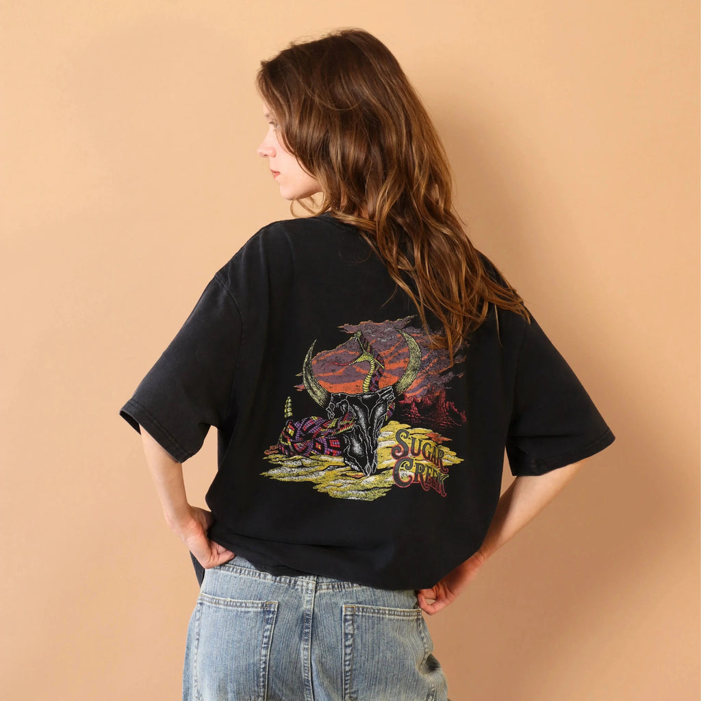 Person wearing a black t-shirt with colorful graphic design on the back against a beige background