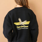 Person wearing a black sweatshirt with a logo on the back against a beige background