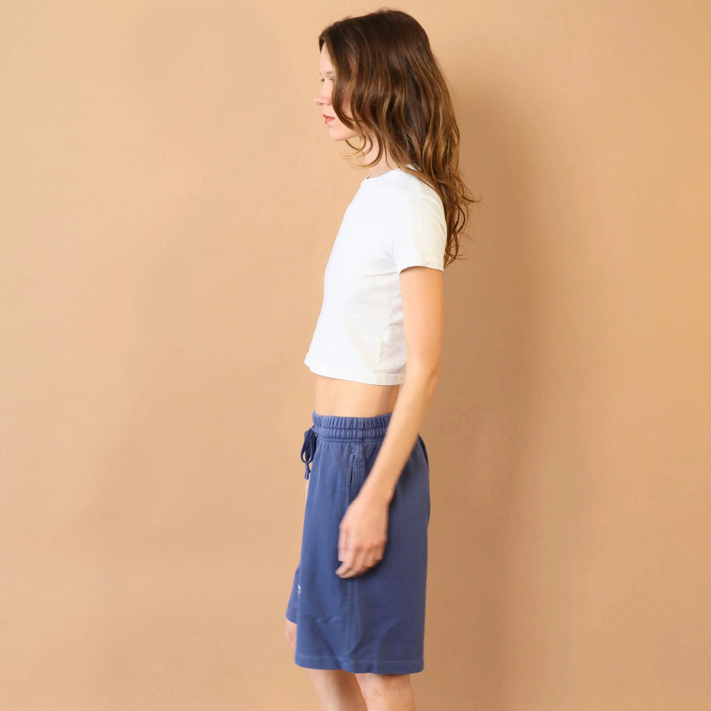 Woman wearing a white top and blue skirt against a beige wall.