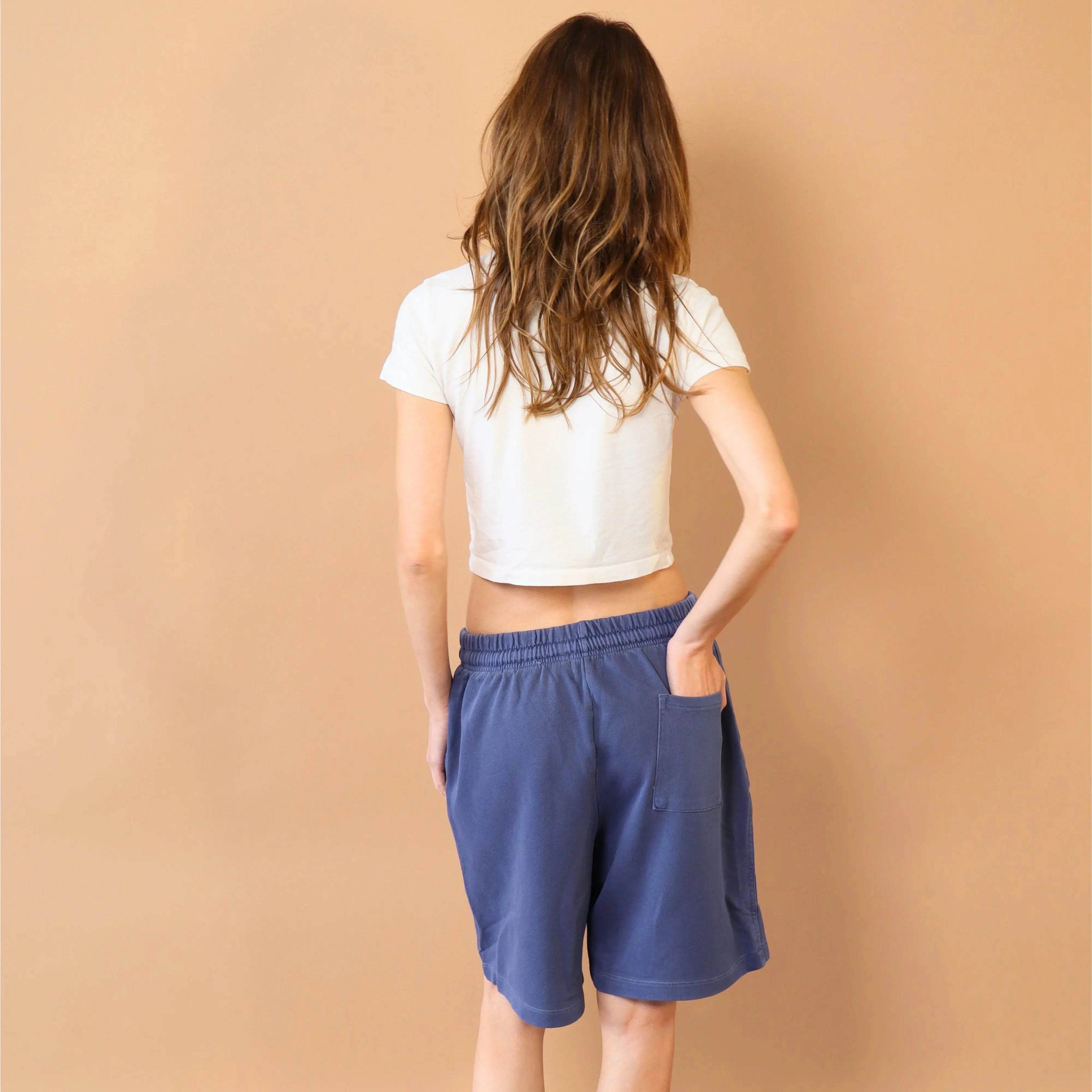 Person wearing a white crop top and blue shorts standing against a beige wall.