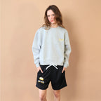 Person wearing a light gray sweatshirt and black shorts with a logo against a beige background
