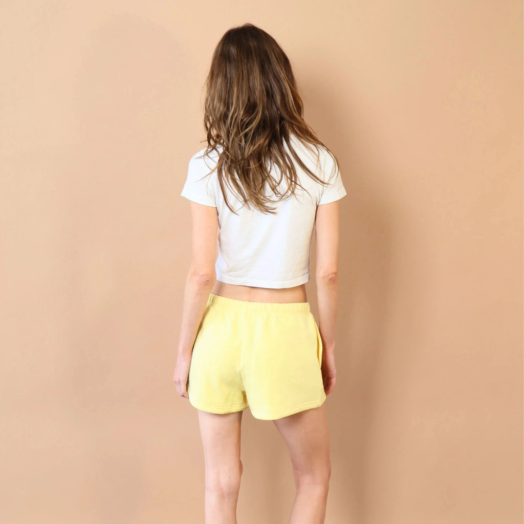 Person wearing a white crop top and yellow shorts against a beige wall.