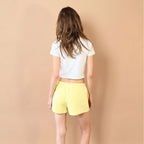 Person wearing a white crop top and yellow shorts against a beige wall.