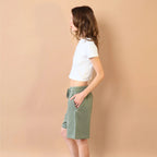 Person wearing a white crop top and green shorts against a beige wall.