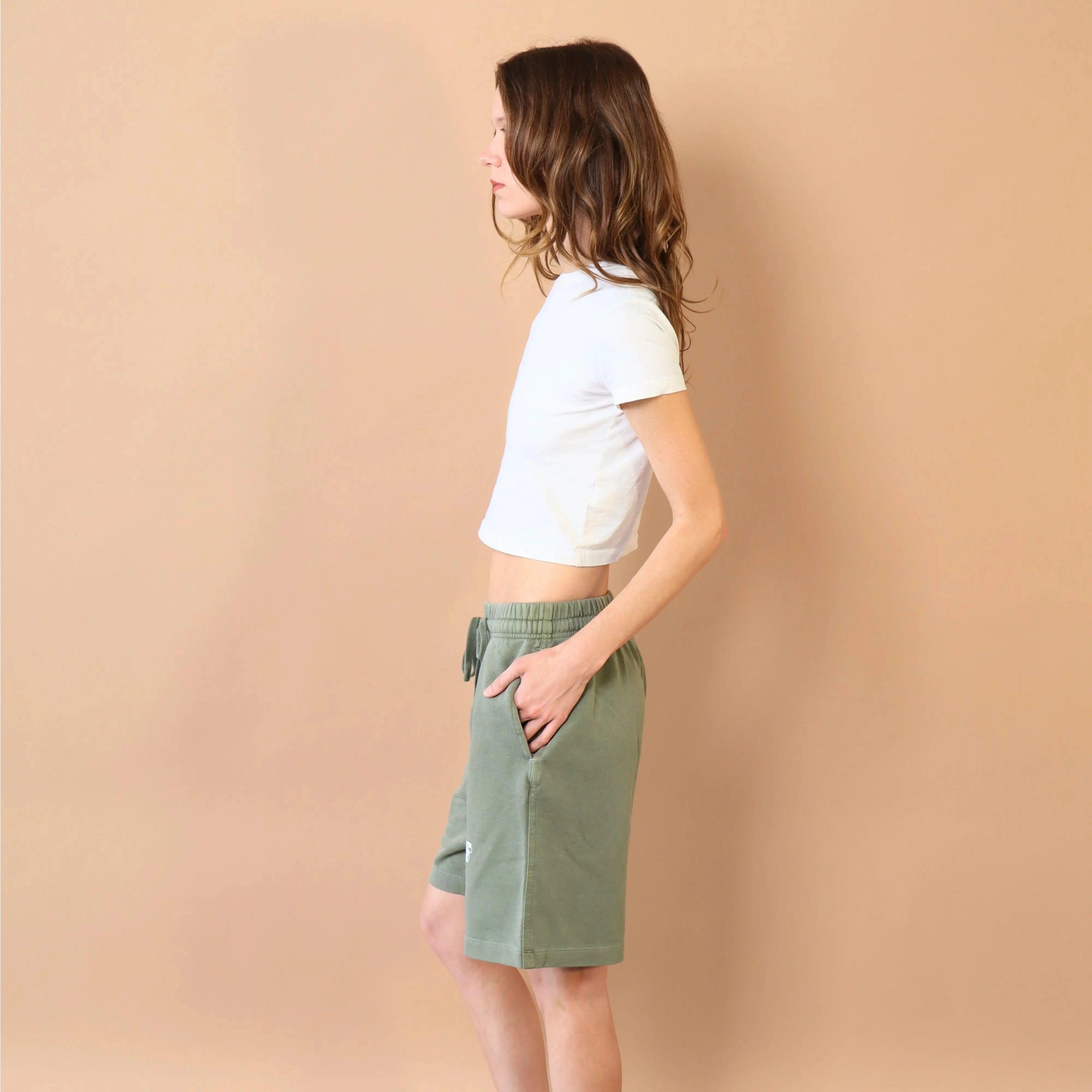 Person wearing a white crop top and green shorts against a beige wall.