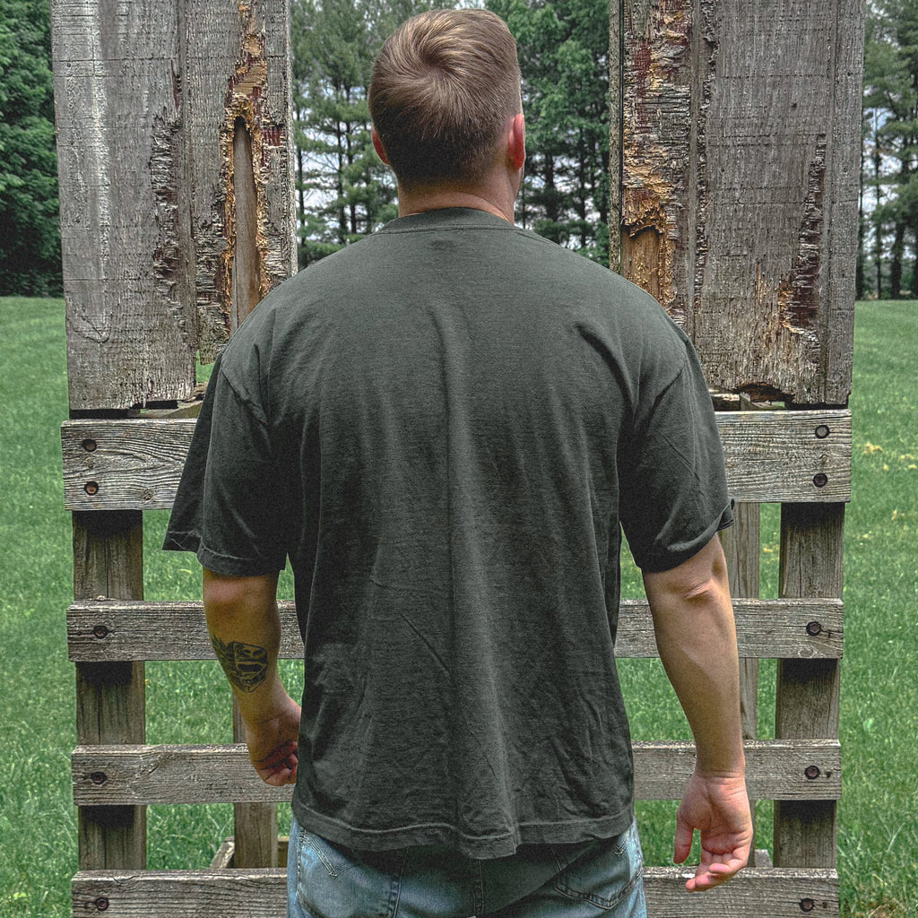 Person wearing a green t-shirt and light blue jeans standing between two wooden pallets in an outdoor setting.